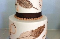 a white wedding cake with brown ribbons, patterns, nuts and painted feathers on the tiers