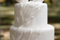 a white plain wedding cake decorated with feathers and with love bird toppers and hearts on them