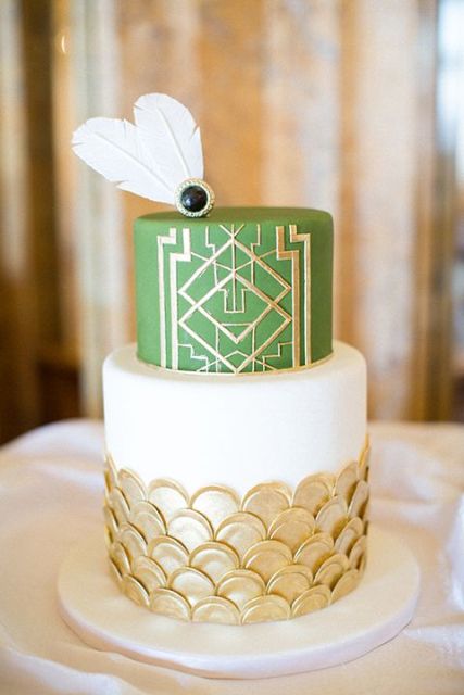 a chic art deco wedding cake with gold scallops, a green and gold geometric tier, white feathers and a black rhinestone