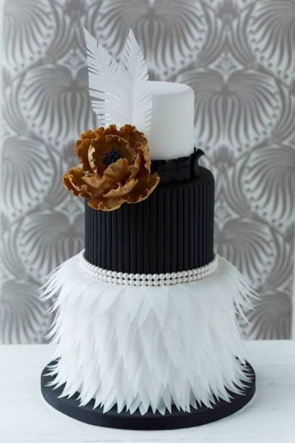 a refined black and white art deco wedding cake with a plain white tier, a striped black one, a white feather one and a gold edible flower