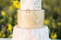 a boho wedding cake with white and gold tiers, with painted dream catchers, feather prints and tier of 3D feathers