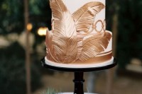 a white and gold wedding cake with stripes and oversized gold feathers looks elegant and chic