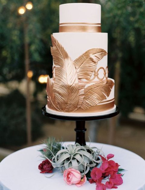 a white and gold wedding cake with stripes and oversized gold feathers looks elegant and chic