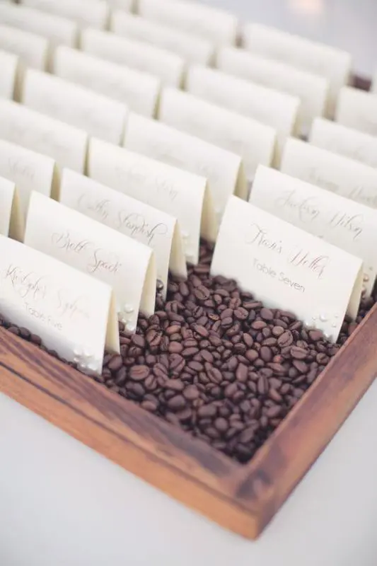 escort cards placed into a wooden box filled with coffee beans is a cool and fresh idea to display them