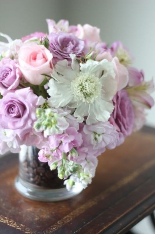 a floral centerpiece of pink and white blooms, with greenery and a sheer vase filled with coffee beans