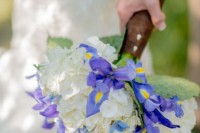 a wedding bouquet of blue irises and white hydrangeas plus greenery and a a brown leather wrap is a cool idea for a bold summer wedding