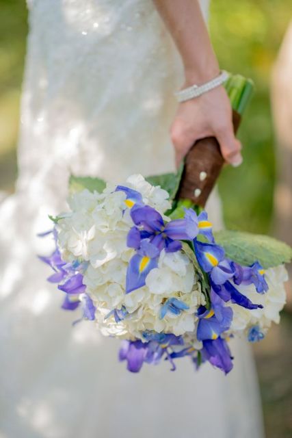a wedding bouquet of blue irises and white hydrangeas plus greenery and a a brown leather wrap is a cool idea for a bold summer wedding