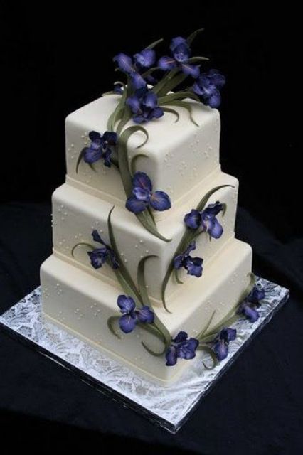 a square white wedding cake with blue irises and greenery is a dramatic idea for a modern wedding with a touch of color