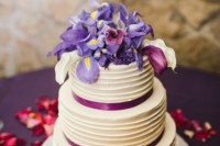 a textural white wedding cake with purple ribbons and white, lilac and purple blooms on top including irises is a fresh idea for spring