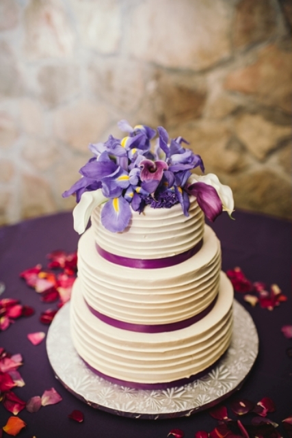 a textural white wedding cake with purple ribbons and white, lilac and purple blooms on top including irises is a fresh idea for spring