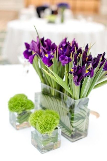 a bold wedding centerpiece of blue irises and moss balls in glasses is a cool idea for a bold summer wedding