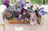 a creative textural wedding centerpiece of a box with white and blue irises, thistles and artichokes is a lovely idea