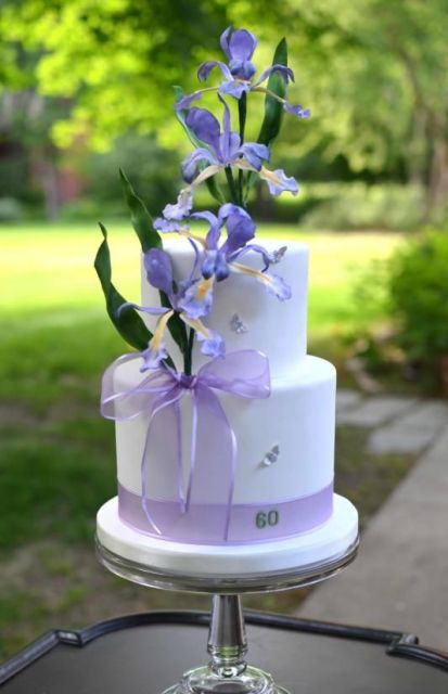 a white wedding cake with a lilac ribbon bow with lots of beautiful blue irises with greenery is a chic idea for a modern spring wedding