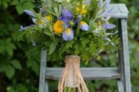 a pretty rustic wedding bouquet of greenery, blue irises and yellow flowers, a lace and twine wrap is a cool and bold idea for a summer wedding