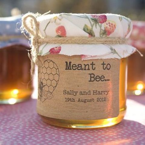 a honey jar with a personalized sticker and a floral cover is a cool idea for a wedding, whether it's a rustic wedding or not