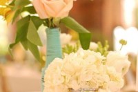 a cute wedding centerpiece of a mint vase with pink blooms and a map covered vase with white flowers for a travel-themed wedding