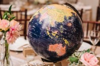 a travel-themed wedding centerpiece of a globe, pink blooms, candles and a stack of books