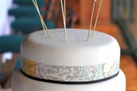 a white wedding cake with map decor and mini map heart cake toppers for a cool and fun look