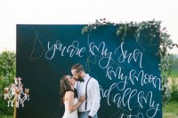 a chalkboard wedding backdrop with greenery and blooms and a quote dedicated to the galaxies and stars