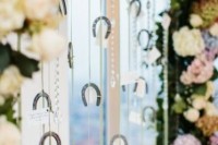 a creative seating chart of a pastel and neutral blooms arch, rhinestones and mini horseshoes that holds cards