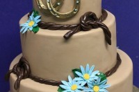 a tan wedding cake with ropes, blue blooms and gold horseshoes is a nice rustic idea