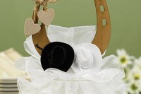 a wedding cake with a plywood horseshoe topper, hats, hearts and a large bow for a rustic wedding