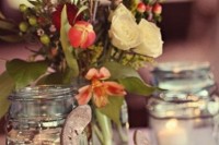 a rustic wedding centerpiece of candles in jars and a simple floral arrangement in a jar
