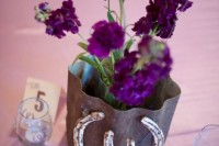 a rustic wedding centerpiece of a metal vase, purple flowers and some horseshoes for a cowboy feel