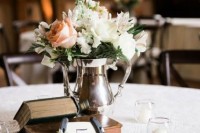 a cool wedding centerpiece of books, a horseshoe with flowers and a silver vase with white and pastel blooms
