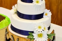 a wedding cake with navy ribbons and white blooms on a stand decorated with horseshoes for a rustic touch