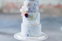a gorgeous four-tier blue ombre marble wedding cake with gold geometric detailing and some blooms is veyr exquisite and bold
