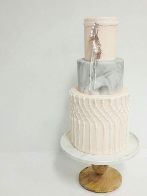 a boho wedding cake with a plain blush, grey marble and blush macrame tier plus some feathers is amazing