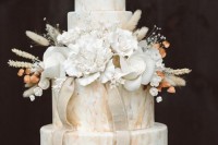 a neutral marble wedding cake with dried, fresh and sugar blooms and some ribbons is a refined wedding dessert idea