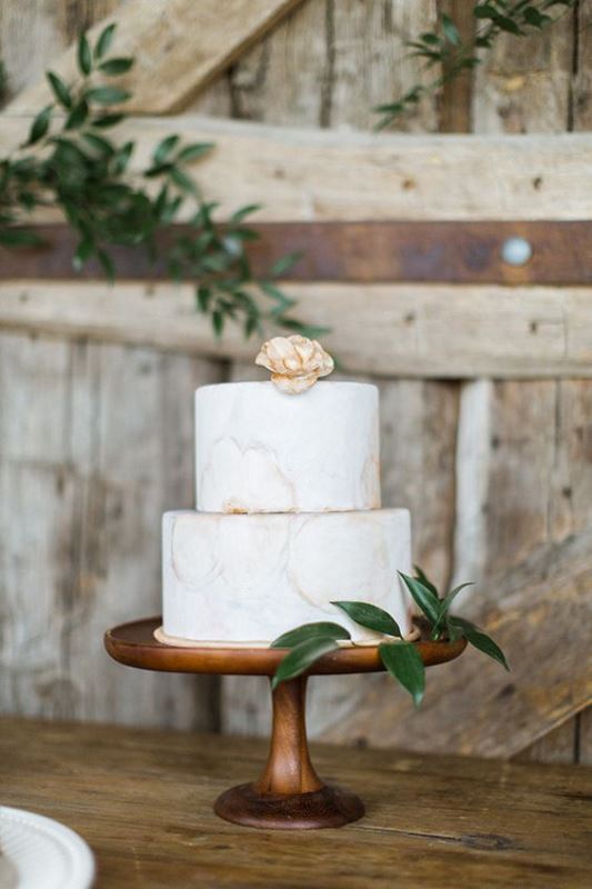 a neutral marble wedding cake decorated with greenery and a sugar bloom is a modern rustic wedding idea