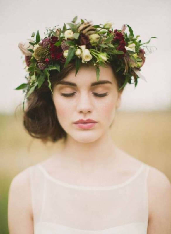 a wavy and a bit messy side low updo with a greenery and moody flower crown for a romantic fall bridal look