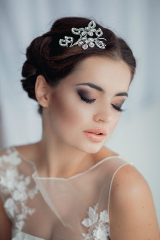 a chic low updo with a bump and a shiny headpiece is a stylish idea for a romantic bride