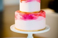 a white wedding cake with bright pink watercolors and gold leaf touches to make it more sparkly and glam