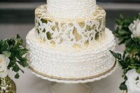 a catchy wedding cake with two ruffle tiers and a single white tier with gold leaf plus some fresh white blooms on top