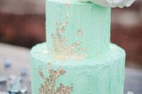 a mint buttercream textural with gold leaf and a large white sugar bloom on top for a spring or summer wedding