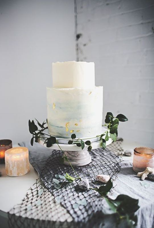 a textural buttercream wedding cake in white and blue watercolors with gold leaf looks very delicate and very chic