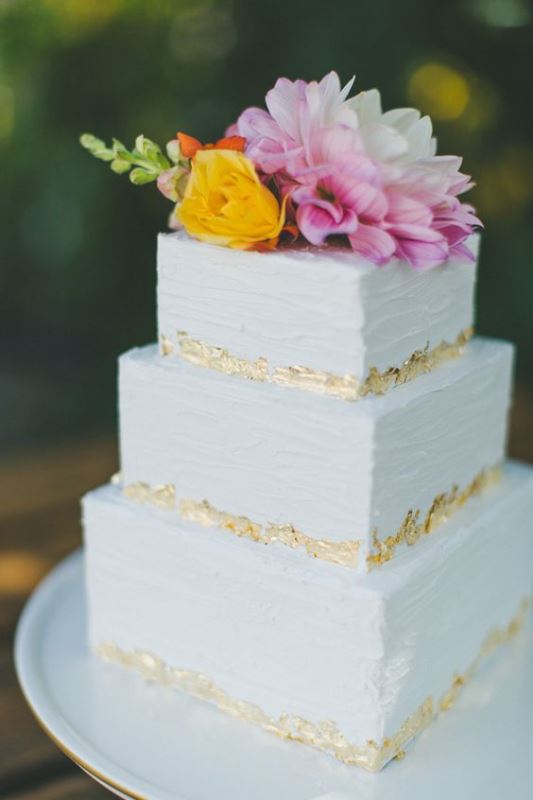 a textural white square wedding cake with gold leaf and bright fresh blooms on top is a cool idea for spring or summer