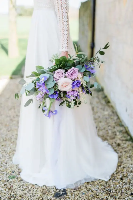 a beautiful wedding bouquet with pale pink roses, blush ones, blue irises and greenery is a very catchy monochromatic arrangement