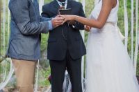 a boho groom outfit with a blue shirt, a tan tie and pants, a grey blazer, two tone boots and a man bun plus hair down