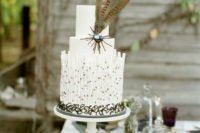 a boho white wedding cake with plain tiers, cookies, some candies and feathers for a boho wedding