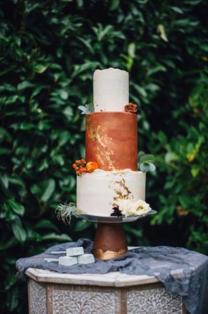 a bold fall wedding cake with textural white and rust tiers, gold leaf, bold and white blooms and some berries