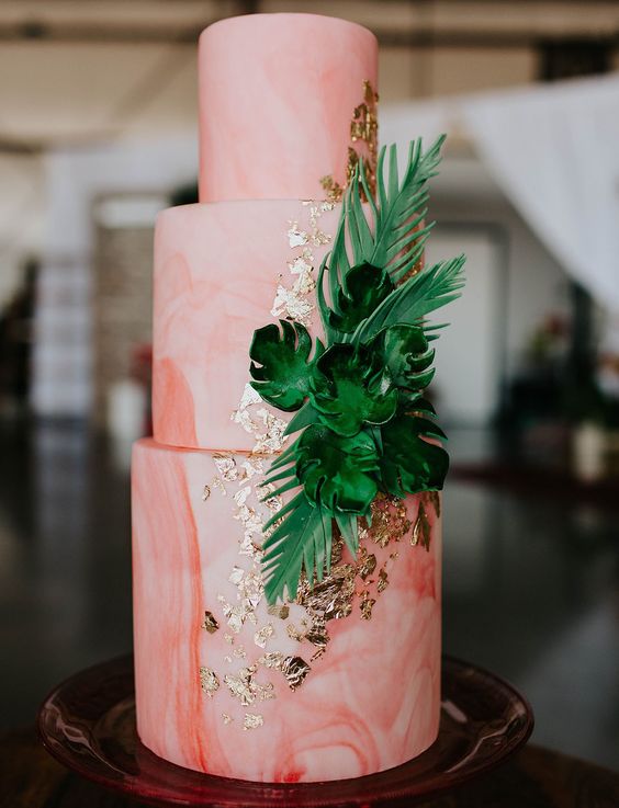 a bold pink watercolor wedding cake with gold leaf and tropical leaves is amazing for a tropical wedding