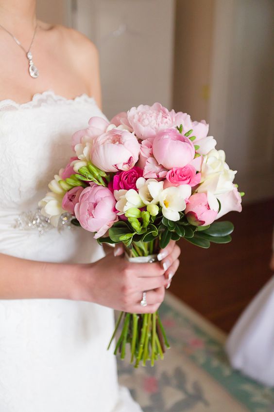 a bold pink wedding bouquet of pink peonies and roses, white freesia, greenery is a lovely touch of color to the bridal look