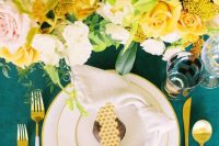 a bold wedding tablescape with an emerald tablecloth, bold yellow, blush and white blooms and greenery and elegant modern cutlery