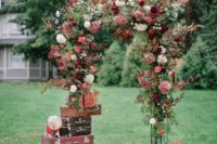 a bright fall wedding arch with a stack of suitcases and globes around for a travel-themed wedding