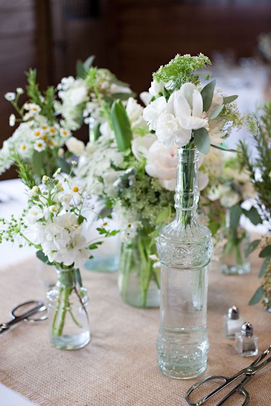 a catchy textural cluster wedding centerpiece of mismatching vases and bottles, white blooms including freesias and greenery